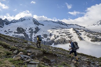 Two mountaineers on a hiking trail, high fog in the valley, glaciated mountains with