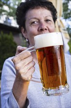 Woman (50-55) with a glass of beer in a beer garden, Prague, Bohemia, Czech Republic, Europe