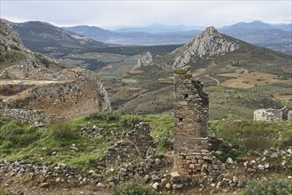 View of crumbling stone walls and ruins in a hilly landscape under a cloudy sky, Archaic Castle,