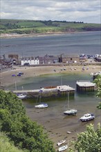 Coastal village with beach, boats and houses surrounded by green countryside, Stonehaven,