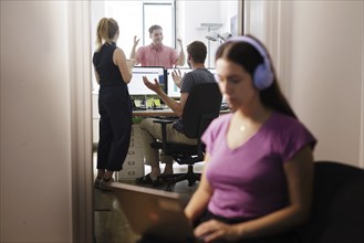 A woman works with headphones on her laptop while colleagues talk loudly. Berlin, 08.08.2024