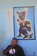 South Ethiopia, in Dimeka, local man sitting in front of a painting in a cafe and smoking a