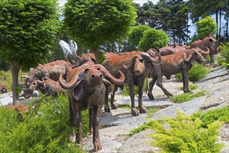 Group of metal sculptures depicting buffaloes in a natural setting with trees and shrubs, Bacalhôa,