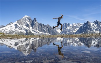 Young man jumping, in front of mountain landscape, reflection in a small mountain lake, mountain