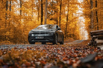 Car driving through autumn forest with orange leaves on a gravel road, electric car, VW ID 5,