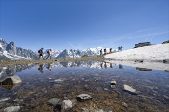 Tourists at Flégère, reflection in a small mountain lake, mountain peaks Grandes Jorasses and Mont