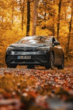 A car driving on a leaf-covered road in an autumn forest, electric car, VW ID 5, Gechingen, Black