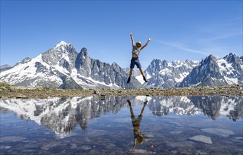 Mountaineer stretches his arms in the air and jumps, in front of mountain landscape, reflection in