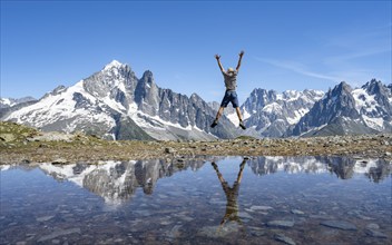 Mountaineer stretches his arms in the air and jumps, in front of mountain landscape, reflection in