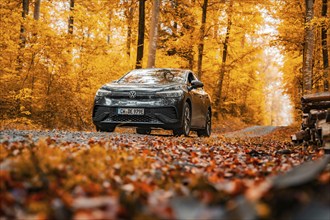 VW ID.4 on a gravel road in an autumnal forest with orange leaves, electric car, VW ID 5,