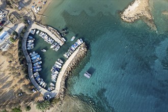 Aerial drone view of fishing harbour and sandy beach. Agia Triada people swimming and fishing boats