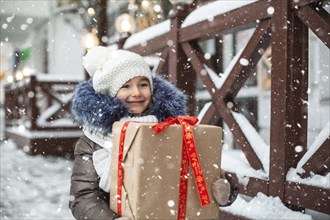 Portrait of joyful girl with a gift box for Christmas on a city street in winter with snow on a