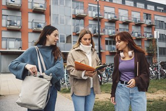 Group of three cheerful female collage students outside their dorm on a cold autumn day, walking on