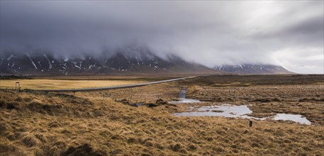 Icelandic countryside with moss on land, empty road and snow mountains in spring