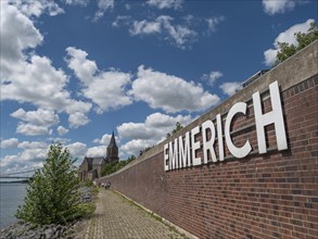 Brick wall with large white lettering, footpath and church in the background, Emmeriich, Rhine,