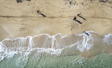 Drone aerial scenery of unrecognised people walking in a sandy beach in winter. Windy waves