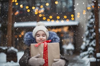 Portrait of joyful girl with a gift box for Christmas on a city street in winter with snow on a