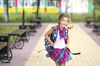 Cheerful girl with a backpack and in a school uniform in the school yard. Back to school, September