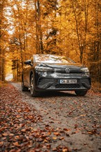 VW ID.4 driving on a gravel road in an autumnal forest with orange leaves, electric car, VW ID 5,