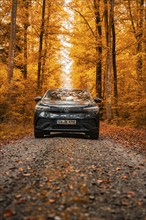 A car drives through an autumn forest on a leaf-covered road, electric car, VW ID 5, Gechingen,