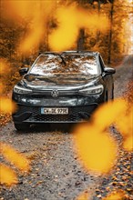 A car on a road in an autumn forest, surrounded by leaves, electric car, VW ID 5, Gechingen, Black