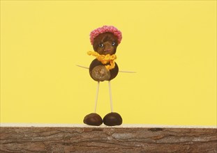 Chestnut figure with hat and scarf in front of yellow background in the studio