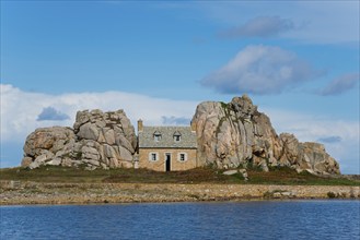 A lonely house between rocky cliffs by the sea and under a blue sky, house between the rocks on the