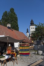 Stand with colourful bales of fabric and woman in medieval traditional costume, in the background