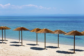 Sandy beach beach with thatched roofs and clear blue sea under a sunny sky, Golden Beach, Pallini,