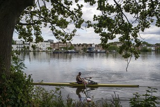 A rower on a river in front of a cityscape with trees and clouds, Royal Botanic Gardens, Kew,