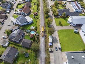 Yellow train runs through the village along the tracks, surrounded by houses and green gardens,