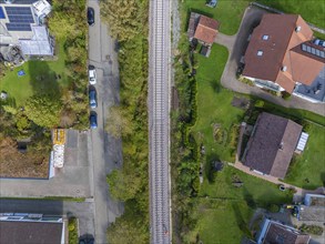 Aerial view of a railway track running through a green residential area, surrounded by houses and