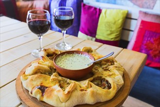 Traditional Georgian adjara round pie with sauce dressing, two wine glasses and sofa with pillows