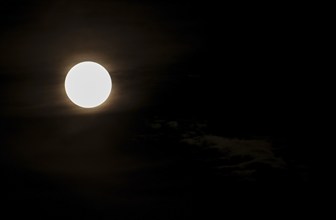 Super bright full moon and partially covered with dramatic black sky clouds