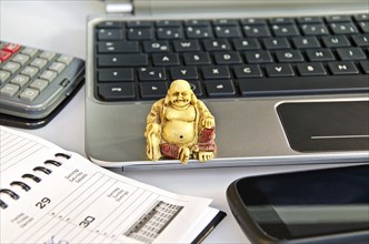 Buddha statue sitting on a laptop in front of office equipment