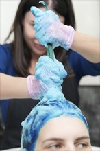 Hairstylist washes female head with dark blue hair color after hair dyeing process in beauty salon.