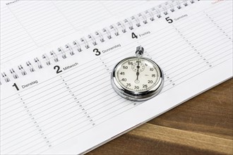 Stopwatch lying on a schedule on a wooden desk (with captions of the days of the week in German)