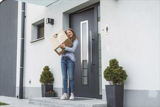 Thrilled caucasian woman standing at the front door with a big cardboard box that just came in the