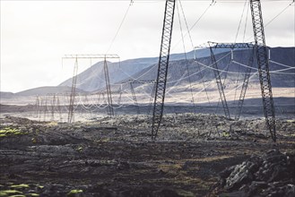 High voltage electrical cables on poles, with a backdrop of a cloudy sky. The lines are attached to