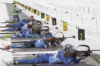 Group sportswoman biathlete aiming, rifle shooting and reloading rifle in prone position.