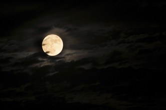 Super bright full moon and partially covered with dramatic black sky clouds