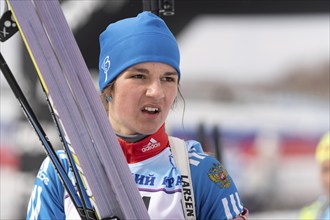 Sportswoman biathlete Soenko Violetta with skis in hands and rifle behind her after skiing and