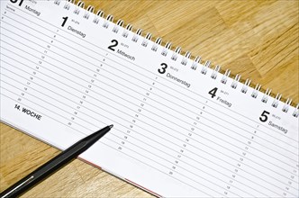 Pen lying on a schedule on a wooden desk (with captions of the days of the week in German)