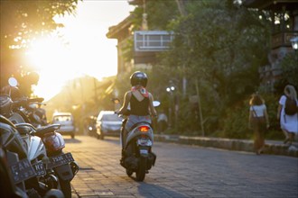 Woman riding a scooter into the setting sun in Ubud, Bali