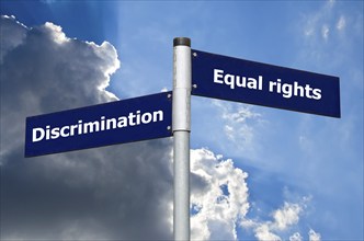 Street sign in front of dark clouds symbolizing crossroads between 'discrimination' and a 'equal