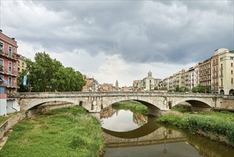 Colorful yellow and orange houses and bridge Pont de Sant Agusti reflected in water river Onyar, in