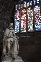 Manchester, England, September 23, 2016: Statue of Humphrey Chetham and colorful stained glass