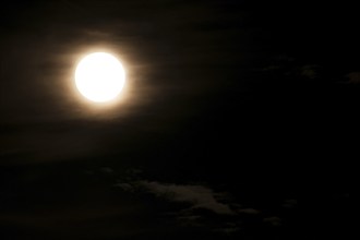 Super bright full moon and partially covered with dramatic black sky clouds