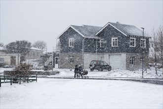 Unrecognized family with kid walking outside during heavy snow storm in Vik village in Iceland