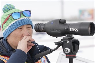 Coach of South Korea biathlon team watches biathletes in monocle at shooting range of biathlon